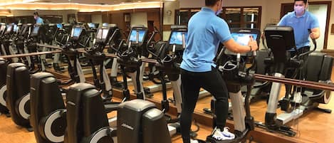 A gym with multiple treadmills, a mirrored wall, and a wooden floor.