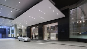 A modern building entrance with a car parked outside, a glass facade, and a large overhang. - New World Makati Hotel (Makati)