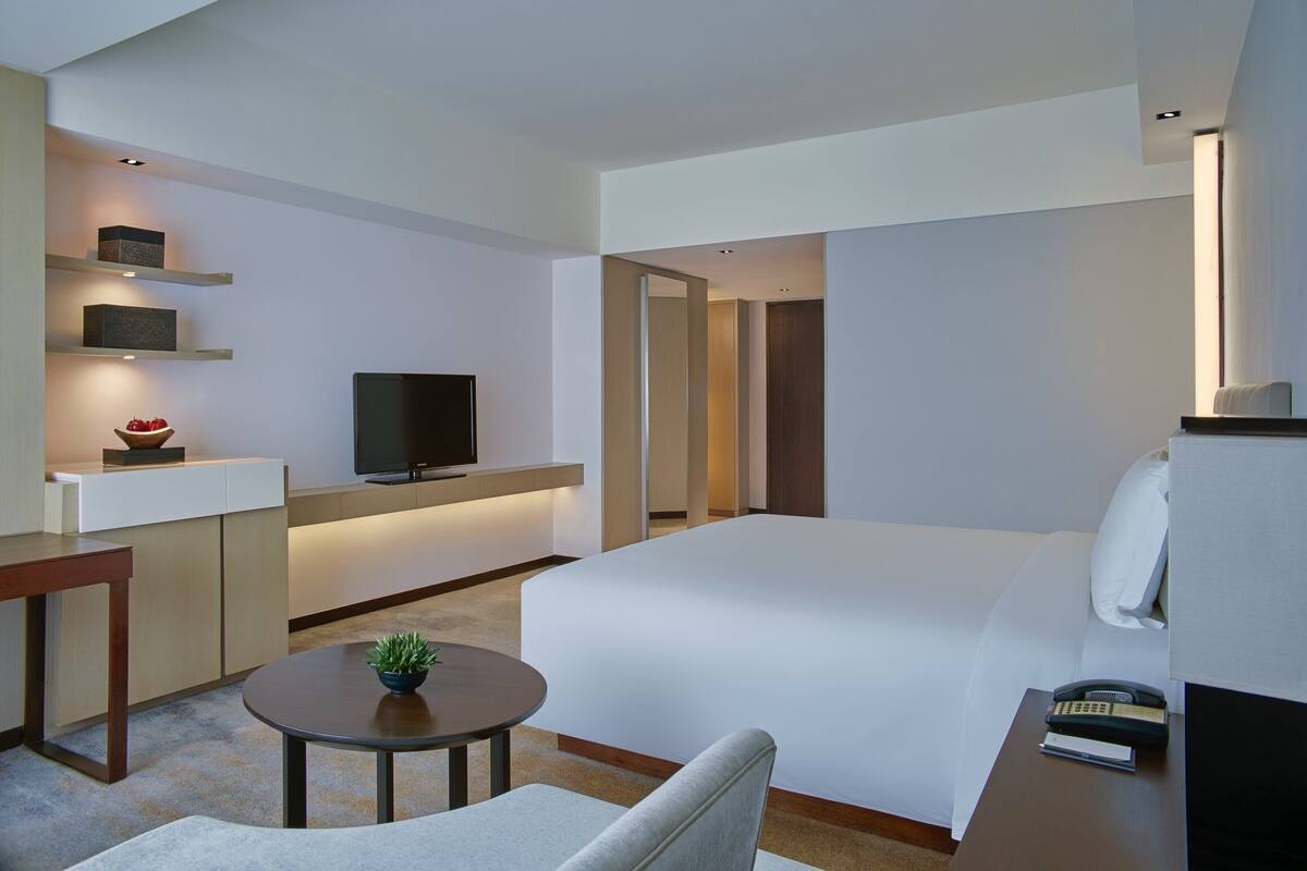 Una habitación de hotel moderna con una cama, un escritorio con televisor de pantalla plana, una mesita con una planta y un teléfono.