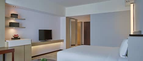 A modern hotel room with a bed, a desk with a flat-screen TV, a small table with a plant, and a telephone.