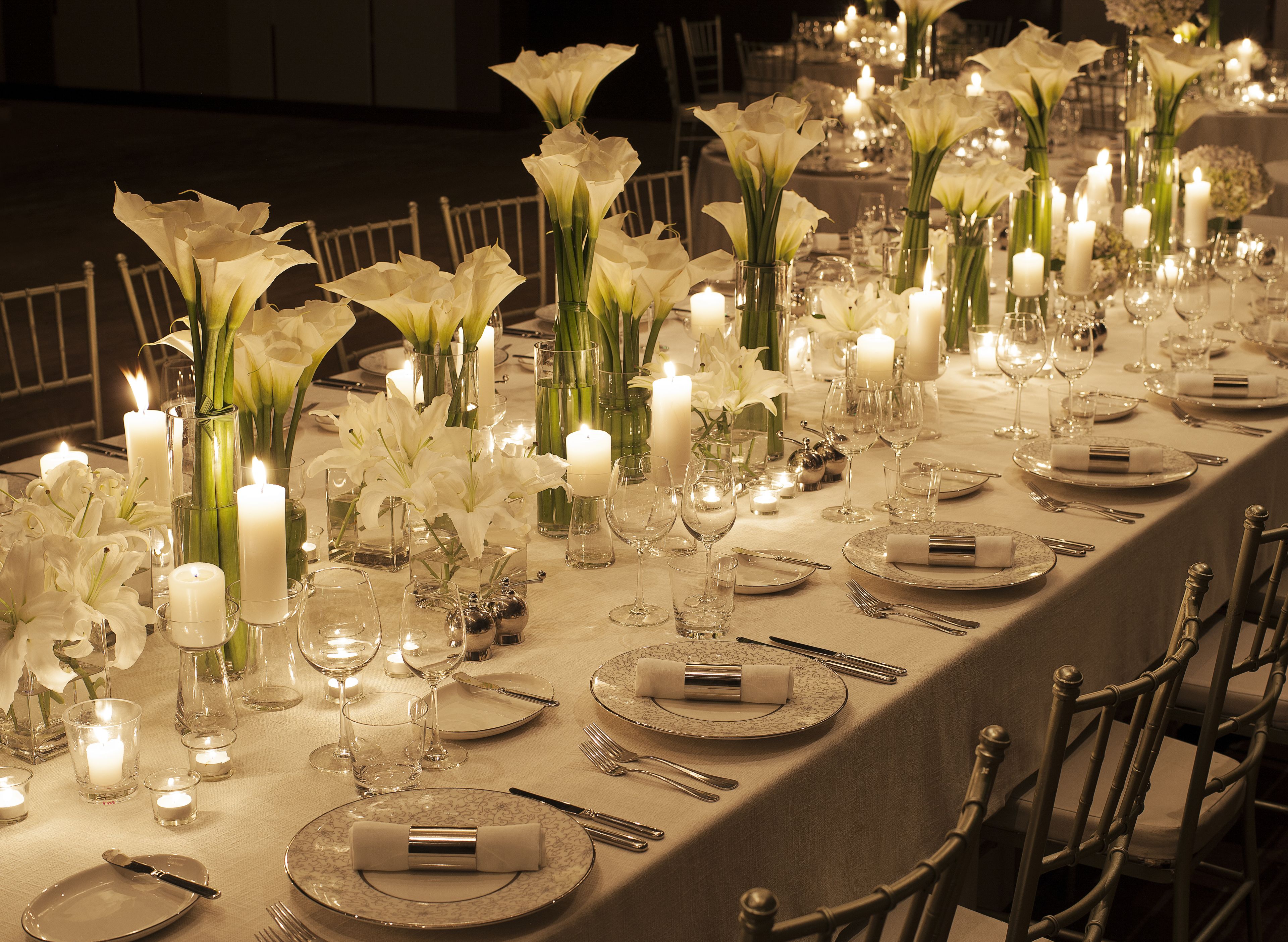 Une longue table à manger, décorée de lys blancs, de bougies et d’une vaisselle élégante.