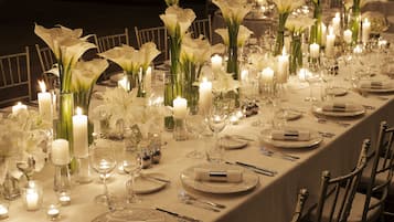 Une longue table à manger, décorée de lys blancs, de bougies et d’une vaisselle élégante.