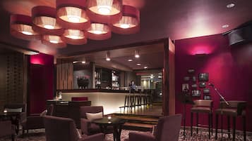 Un salon à l’éclairage tamisé, doté de fauteuils confortables et d’un bar en arrière-plan.