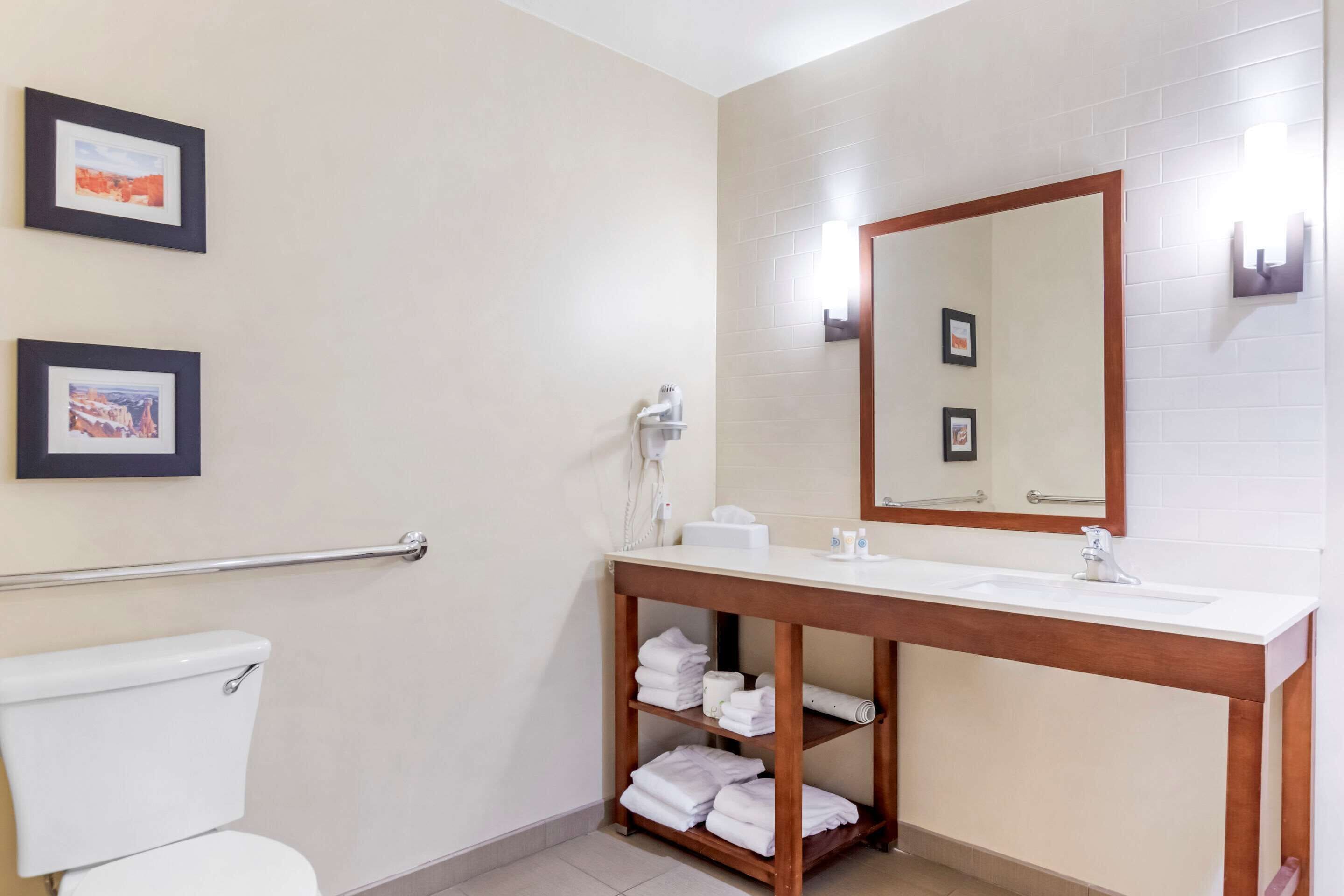 A bathroom with a toilet, a sink with a mirror, and shelves with towels.