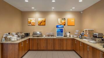 A modern hotel kitchen with wooden cabinets, a coffee station, and a self-serve breakfast area.