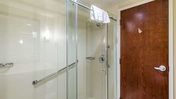 A glass-enclosed shower with a white towel hanging on the door handle, a wooden door with a silver handle, and a metal grab bar.