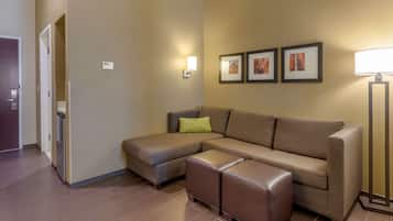 A modern living room with a sectional sofa, a small ottoman, a standing lamp, and framed artwork on the wall.