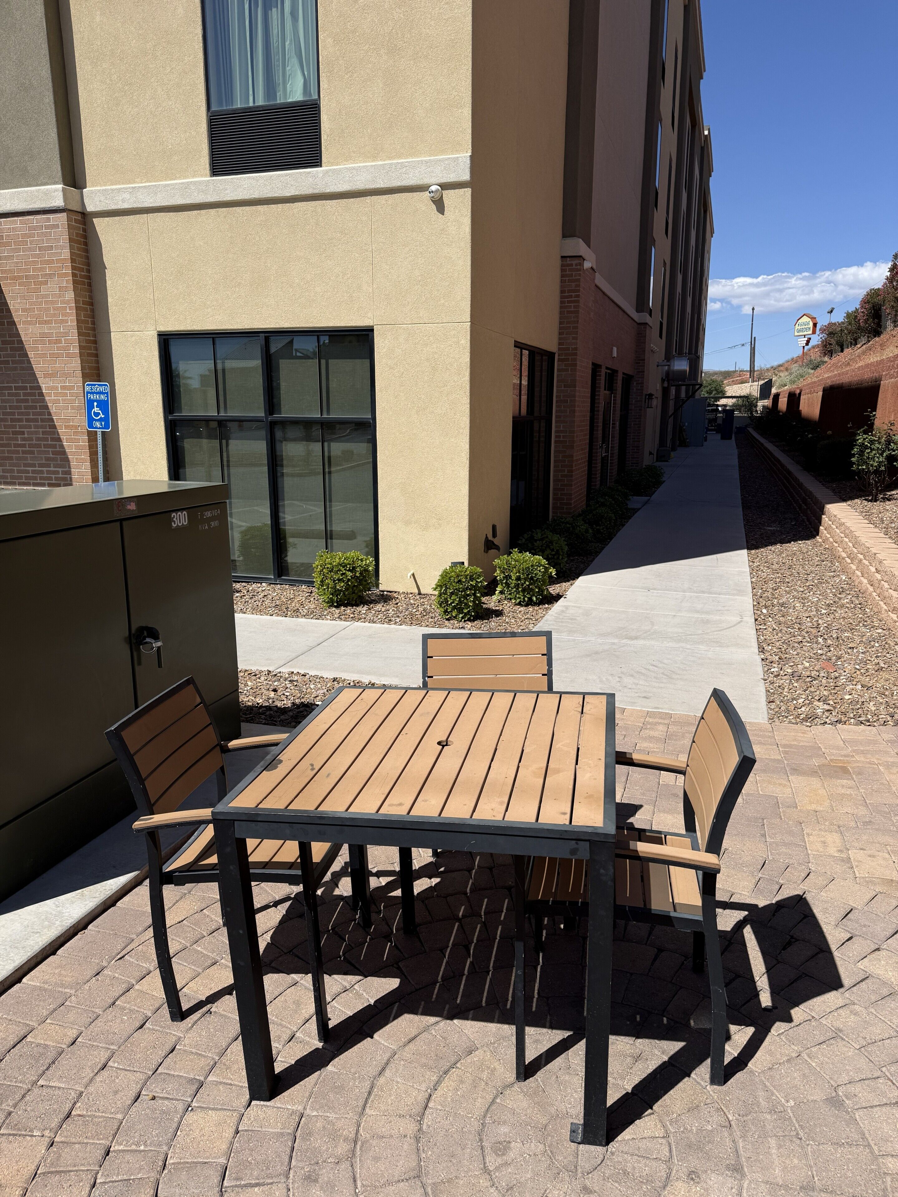 Un patio con mesa y sillas, un cartel de estacionamiento reservado y un edificio con ventanales grandes.