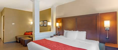 A hotel room with a large bed, a nightstand, a lamp, a sofa, and a mirror.