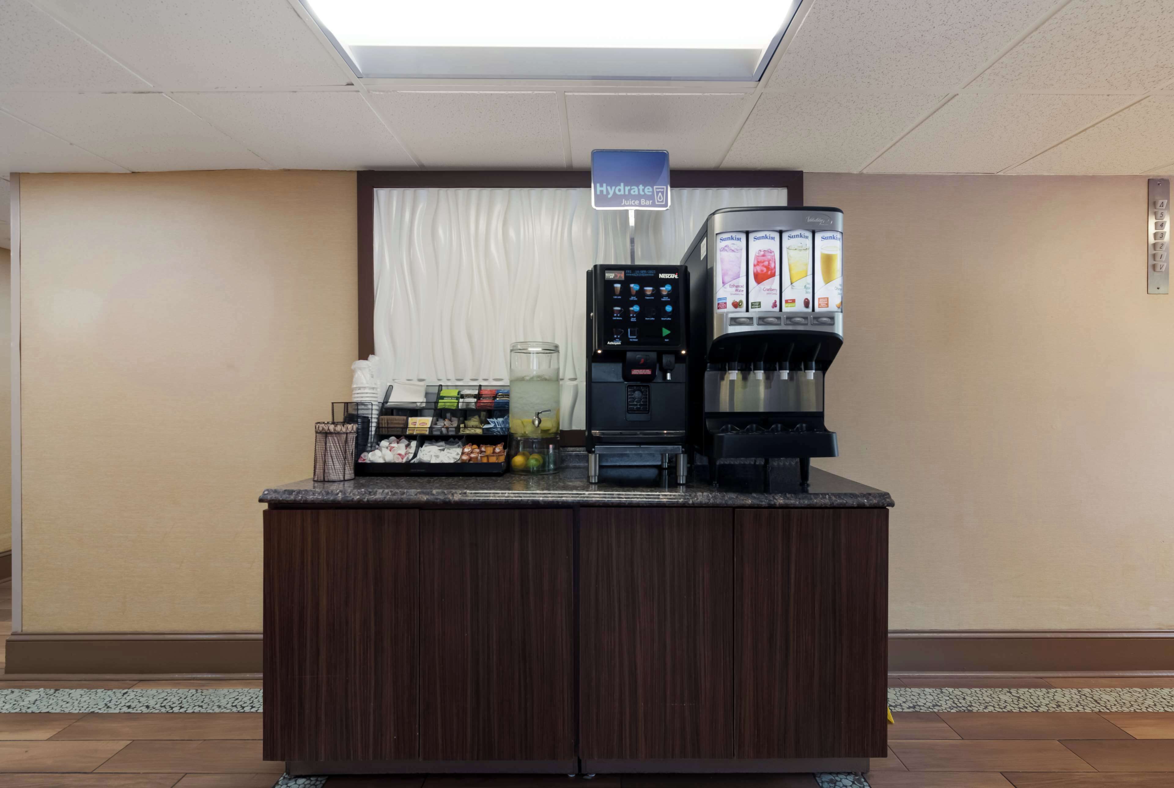 Uma área de recepção de hotel com um bar de sucos, uma máquina de café e um dispensador de bebidas.