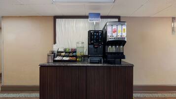 Uma área de recepção de hotel com um bar de sucos, uma máquina de café e um dispensador de bebidas.