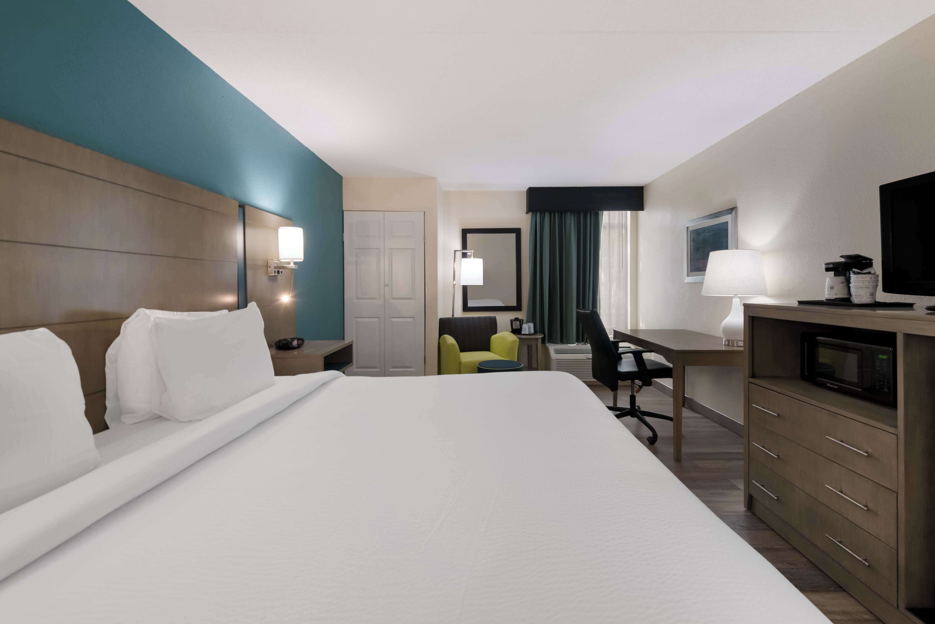 A hotel room with a large bed, a desk, a chair, a television, and a minibar.