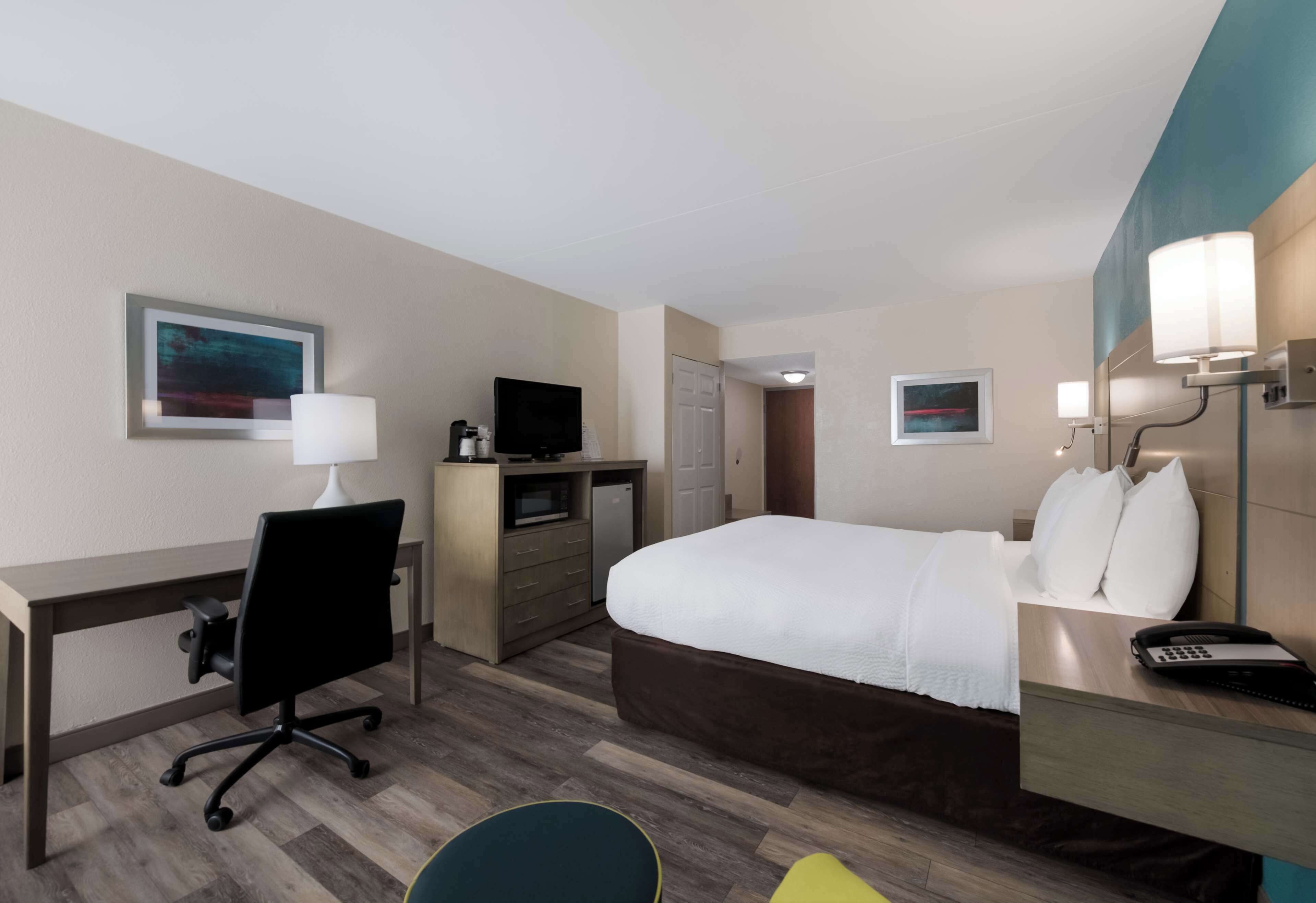 A hotel room with a bed, desk, chair, TV, and a small kitchenette.