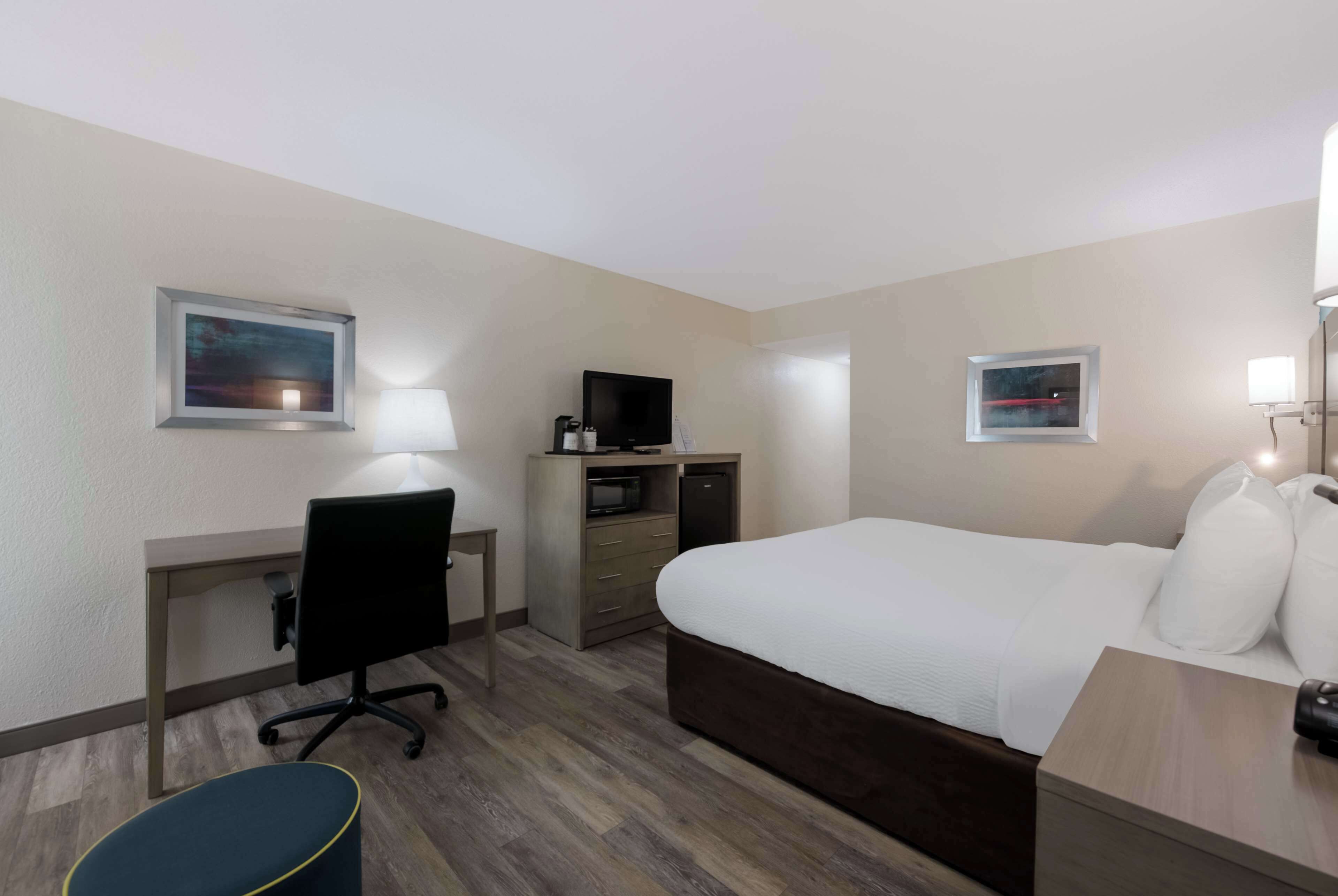 A hotel room with a bed, desk, chair, television, and artwork on the walls.