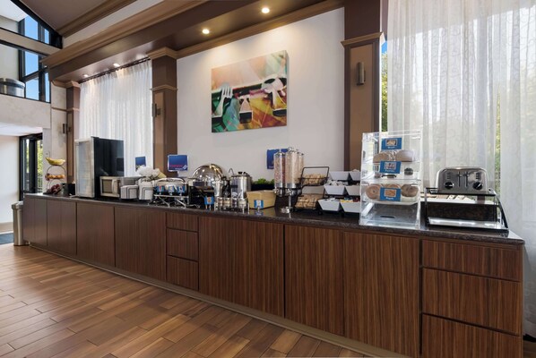 A breakfast bar with coffee machines, a fruit bowl, and a decorative painting. - Best Western Hampton Coliseum Inn (Hampton)