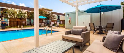 Zona junto a la piscina con sillones, una mesa y sombrillas.