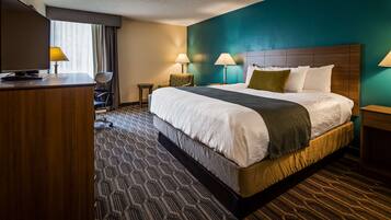 A hotel room with a large bed, two bedside lamps, a desk with a TV, and a chair.