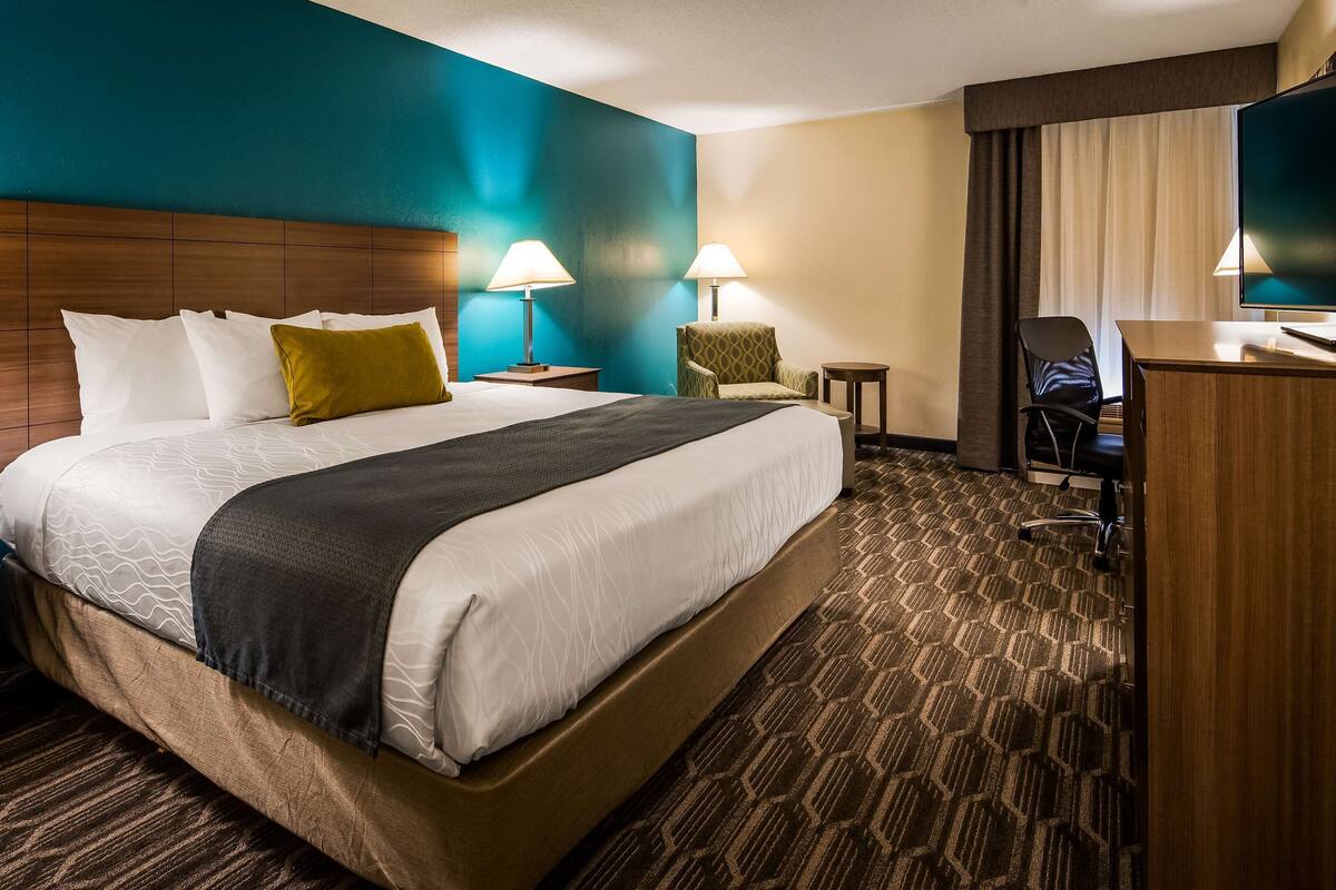 A hotel room with a large bed, two bedside tables, a desk, a chair, and a television.