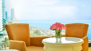 A room with a view of the ocean and city skyline, featuring a table with a vase of flowers and two armchairs. - The Kingsbury Colombo (Colombo)