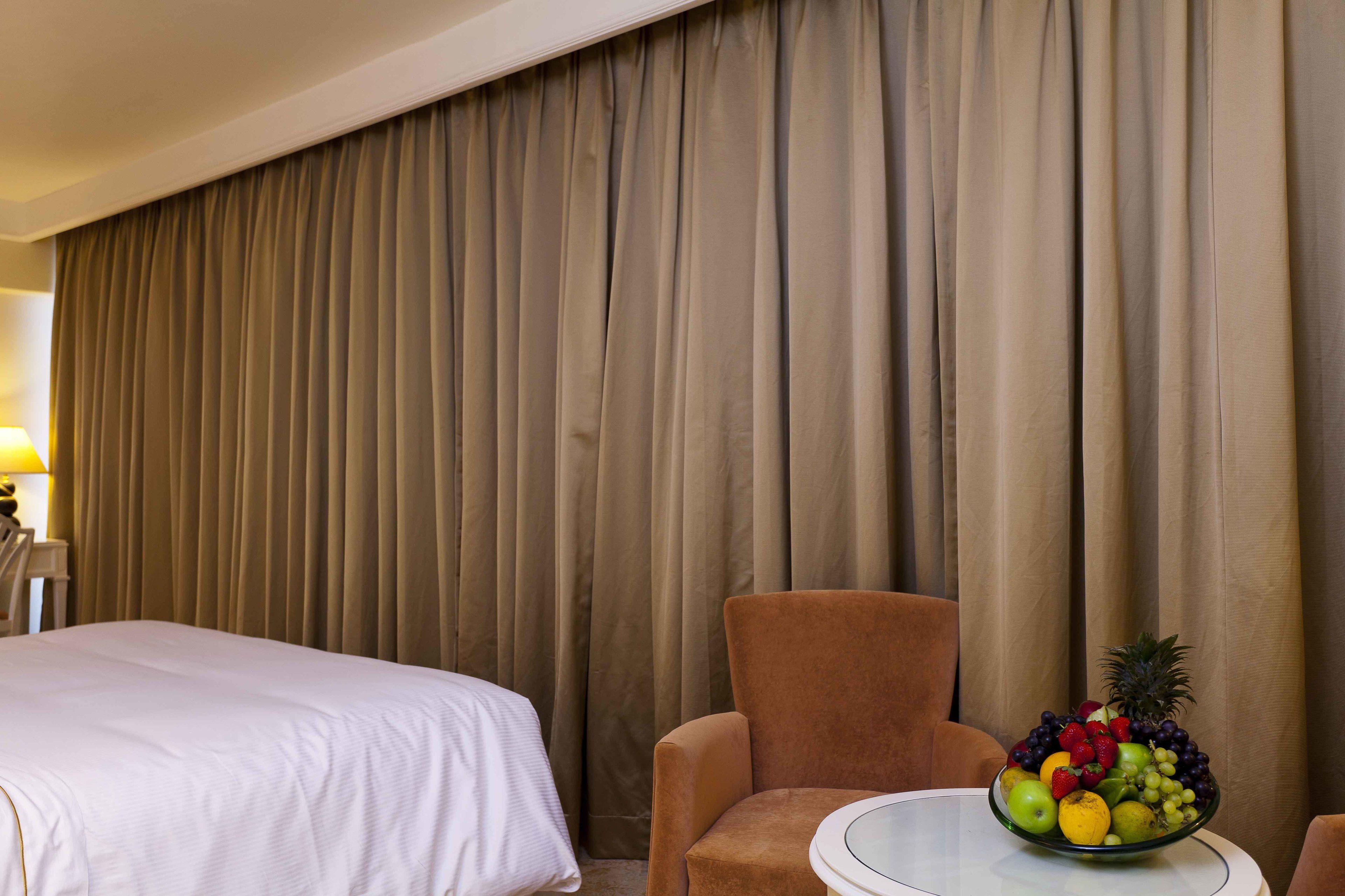 A hotel room with a bed, a brown armchair, and a table with a fruit bowl.