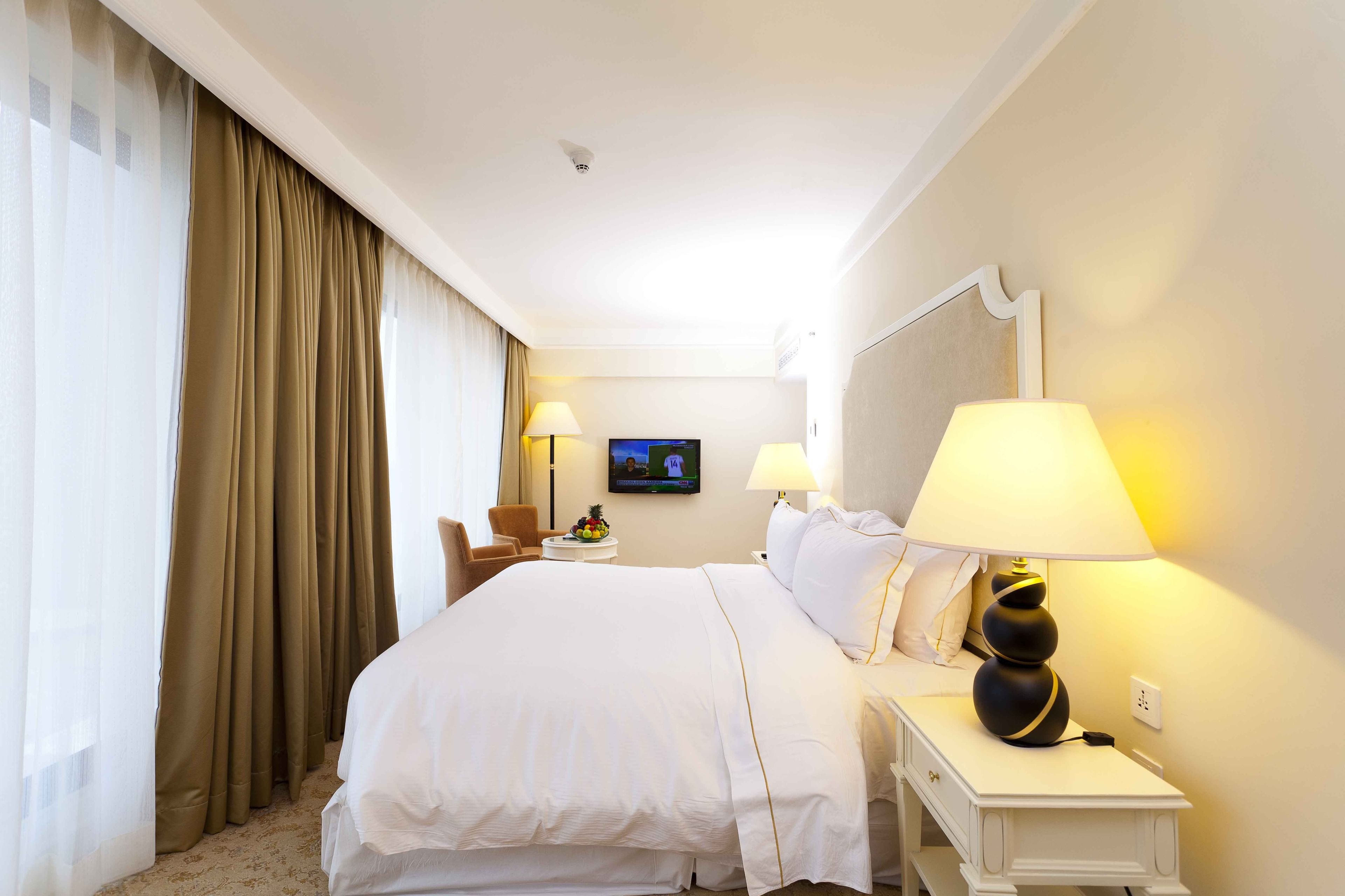 Habitación de hotel con una cama grande, dos lámparas de noche, un televisor en la pared y una pequeña mesa con frutero.