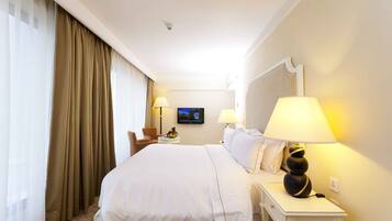 Habitación de hotel con una cama grande, dos lámparas de noche, un televisor en la pared y una pequeña mesa con frutero.