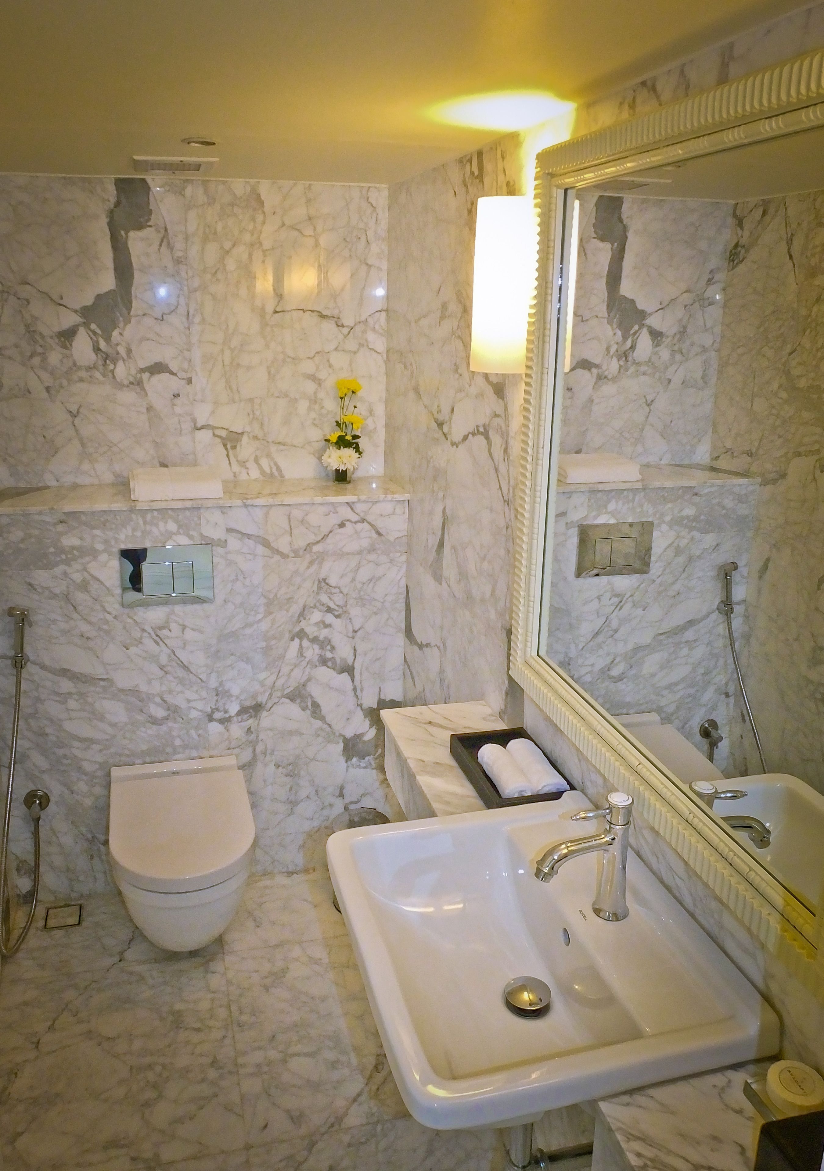 A bathroom with a marble wall, a toilet, a sink, and a shower.