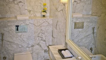 A bathroom with a marble wall, a toilet, a sink, and a shower.