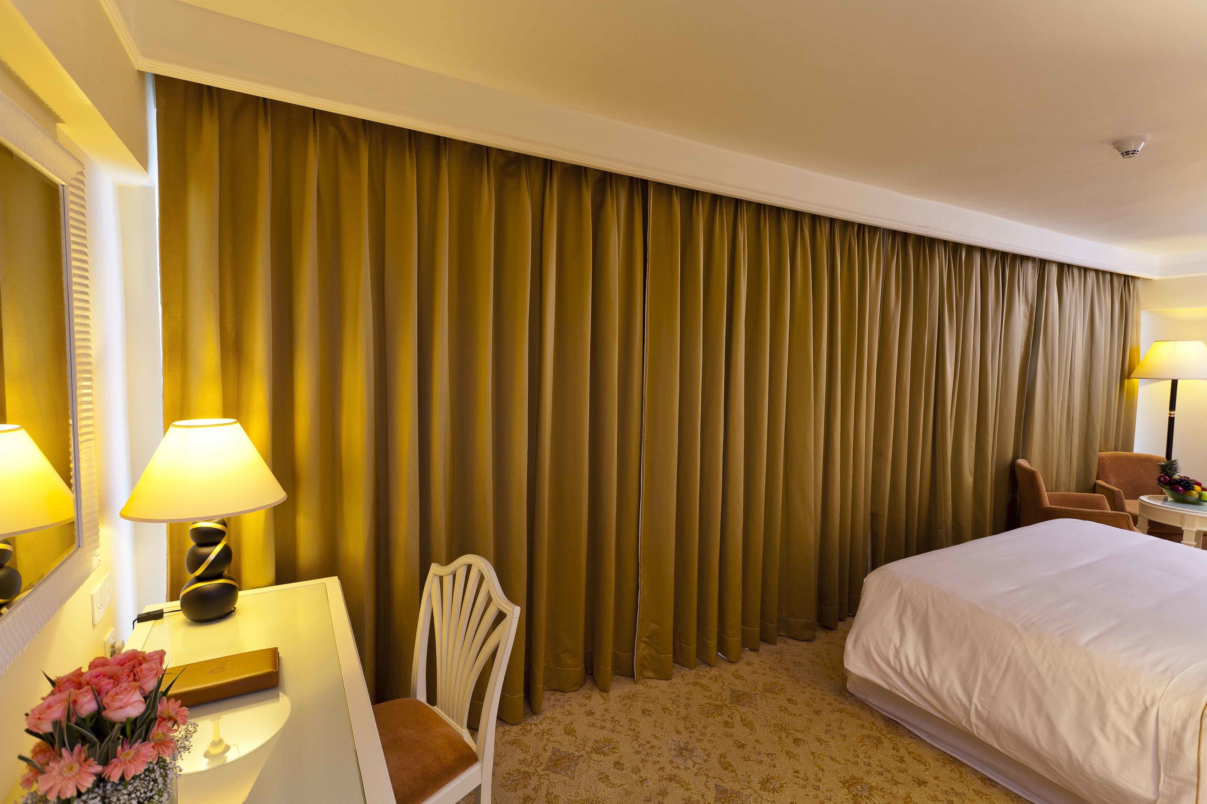 Una habitación de hotel con una cama grande, un escritorio con lámpara, una silla y una cortina.