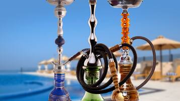Tres cachimbas sobre una mesa, con una playa y sombrillas al fondo.