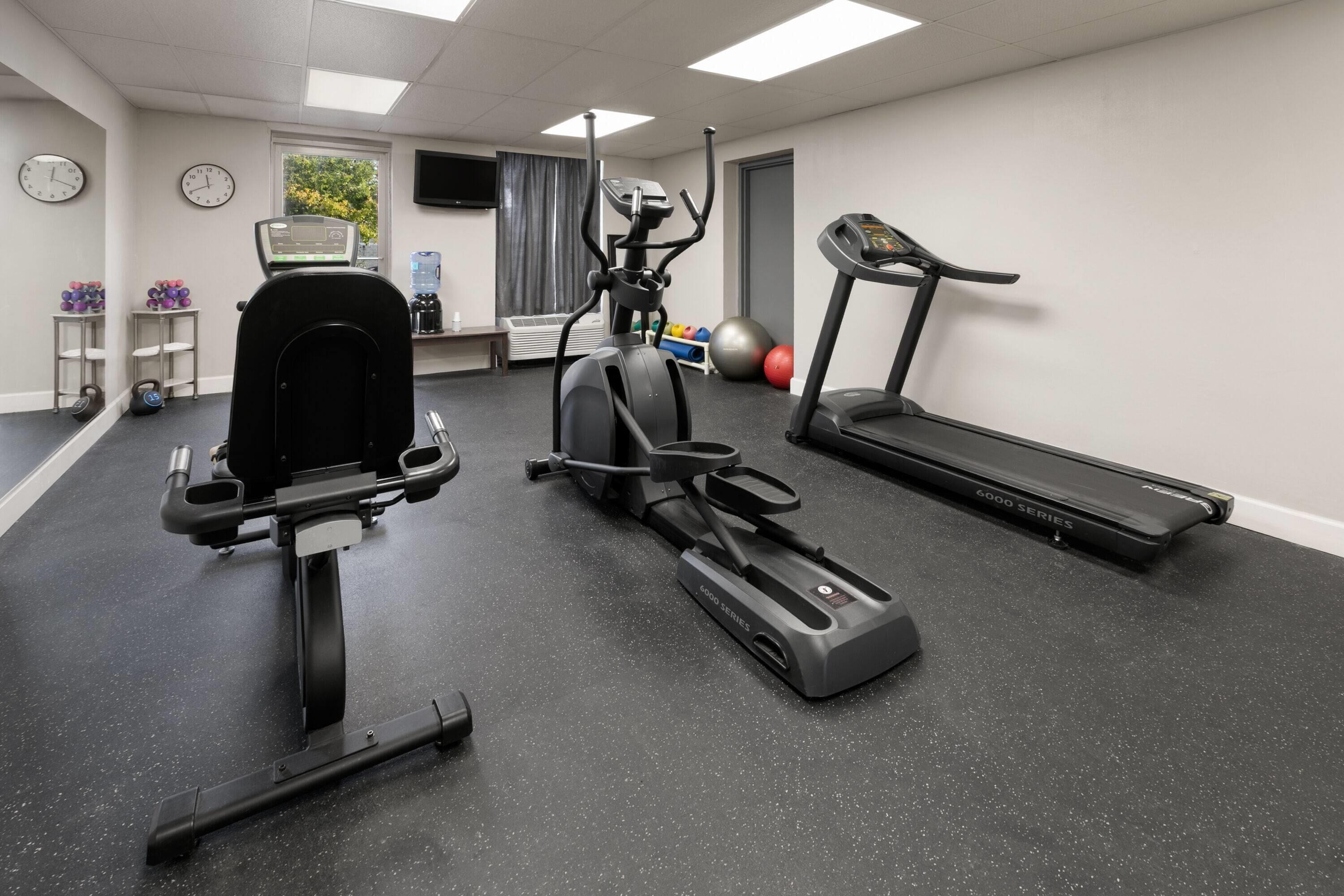 A gym with a stationary bike, elliptical, treadmill, and weights.