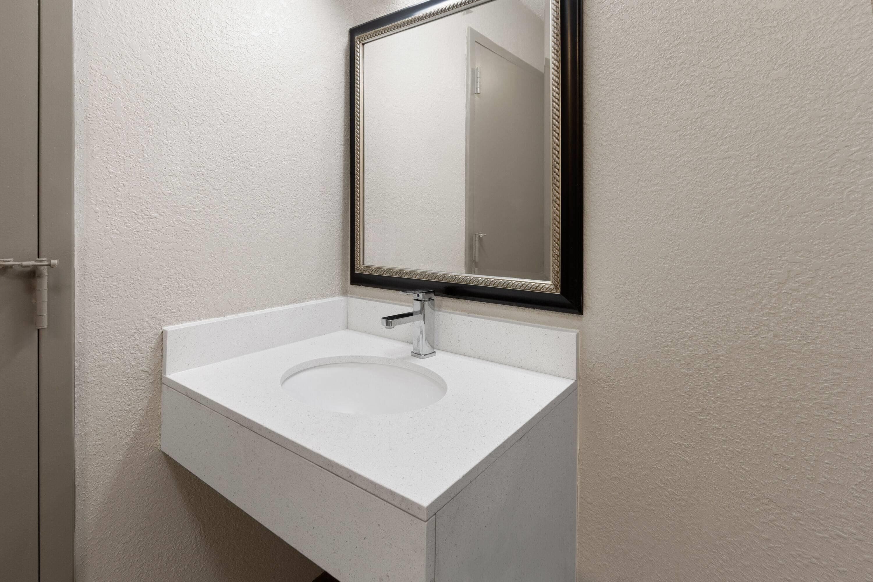 Een badkamer met een witte wastafel, een spiegel met een zwarte lijst en een deur.