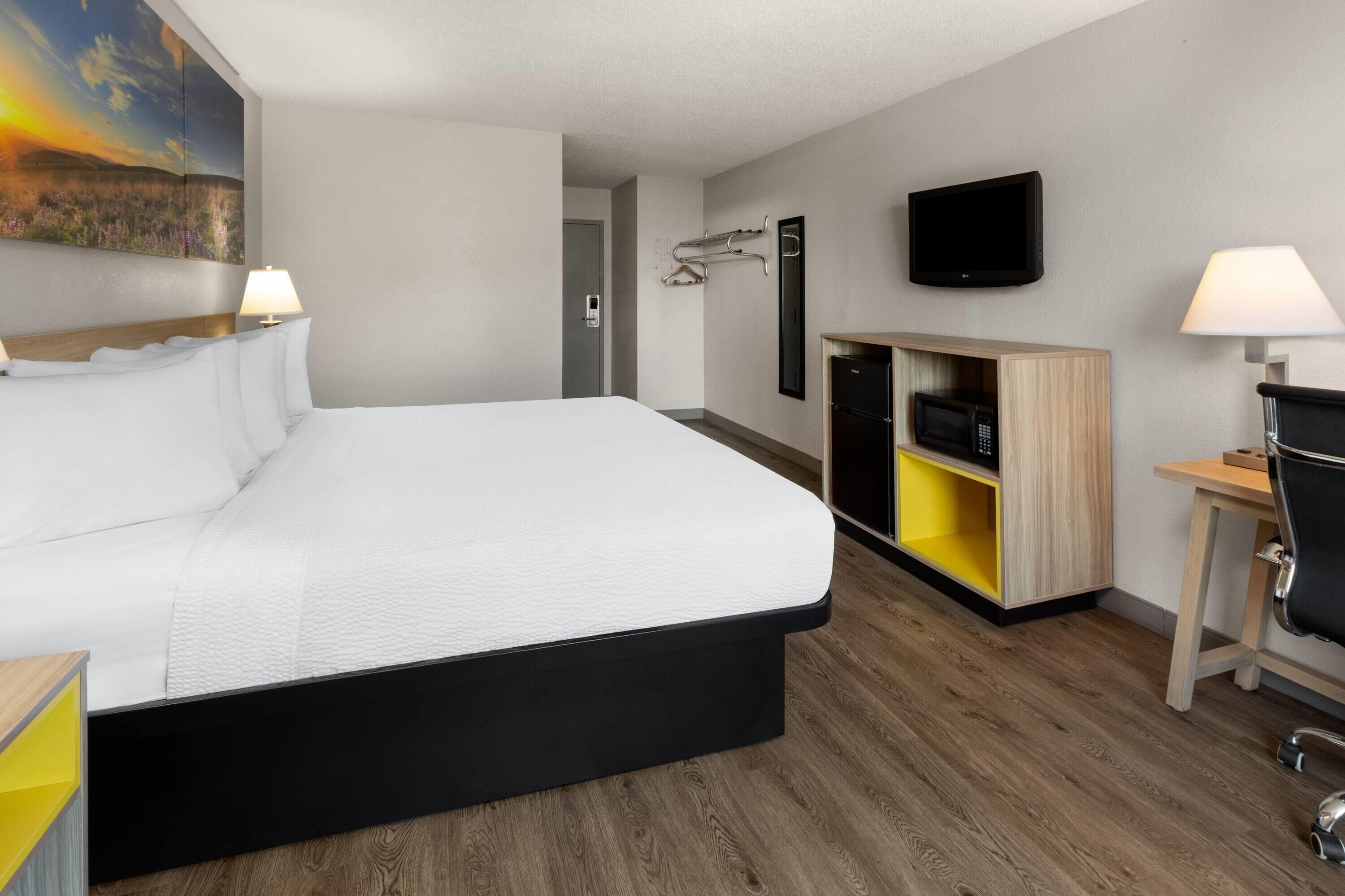 A modern hotel room with a large bed, a desk with a chair, a TV, and a microwave.
