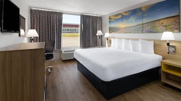 A hotel room with a large bed, a desk, a chair, a TV, and a painting on the wall.
