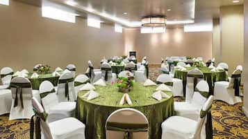 A banquet hall with round tables covered in green tablecloths, white chairs with green sashes, and a chandelier.