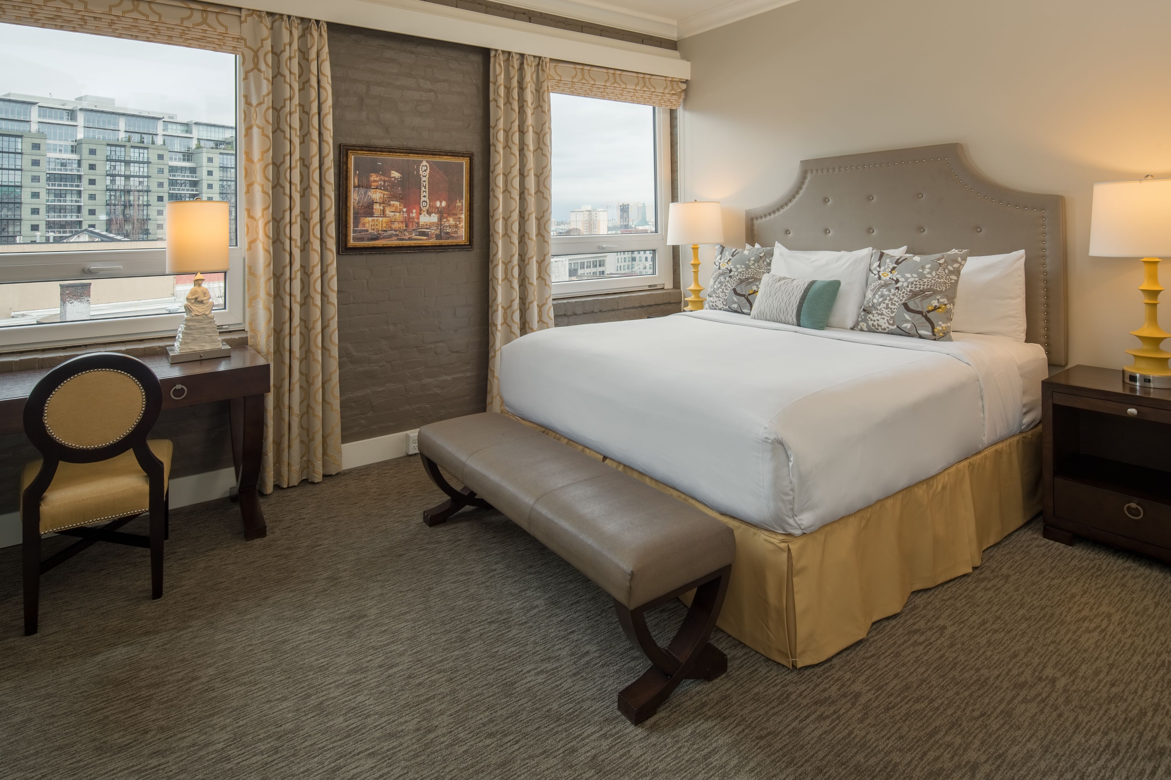 Una habitación de hotel con una cama grande, un banco, un escritorio y vistas a la ciudad.