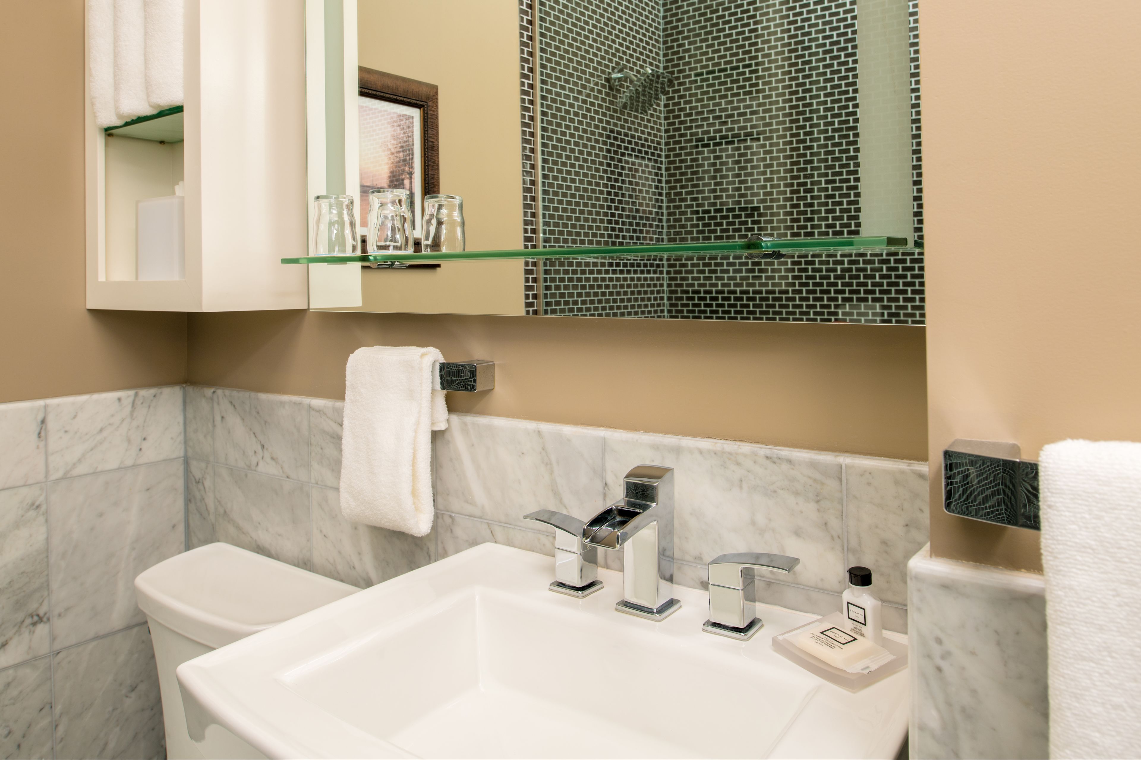 A bathroom with a white sink, two faucets, a mirror, and a shower area with mosaic tiles.