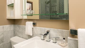 A bathroom with a white sink, two faucets, a mirror, and a shower area with mosaic tiles.