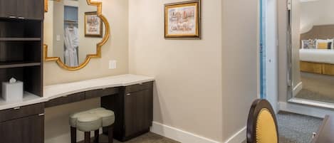 A hotel room with a vanity, a mirror, a framed picture, a bed, and a chair.