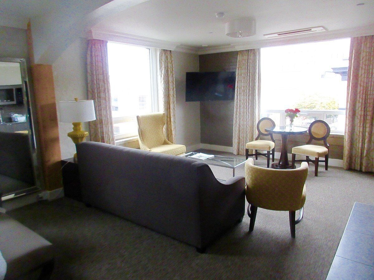 Habitación de hotel con sofá, sillones, una mesa de centro, televisor y balcón con cortinas.