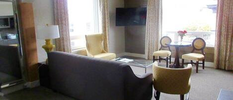 Habitación de hotel con sofá, sillones, una mesa de centro, televisor y balcón con cortinas.