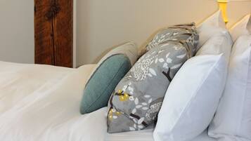 A neatly made bed with white linens and a variety of pillows, including floral and solid colors.