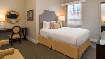 A hotel room with a large bed, a desk with a chair, a mirror, and a window with curtains.