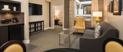 A modern hotel room with a dining area, a sofa, and a television.
