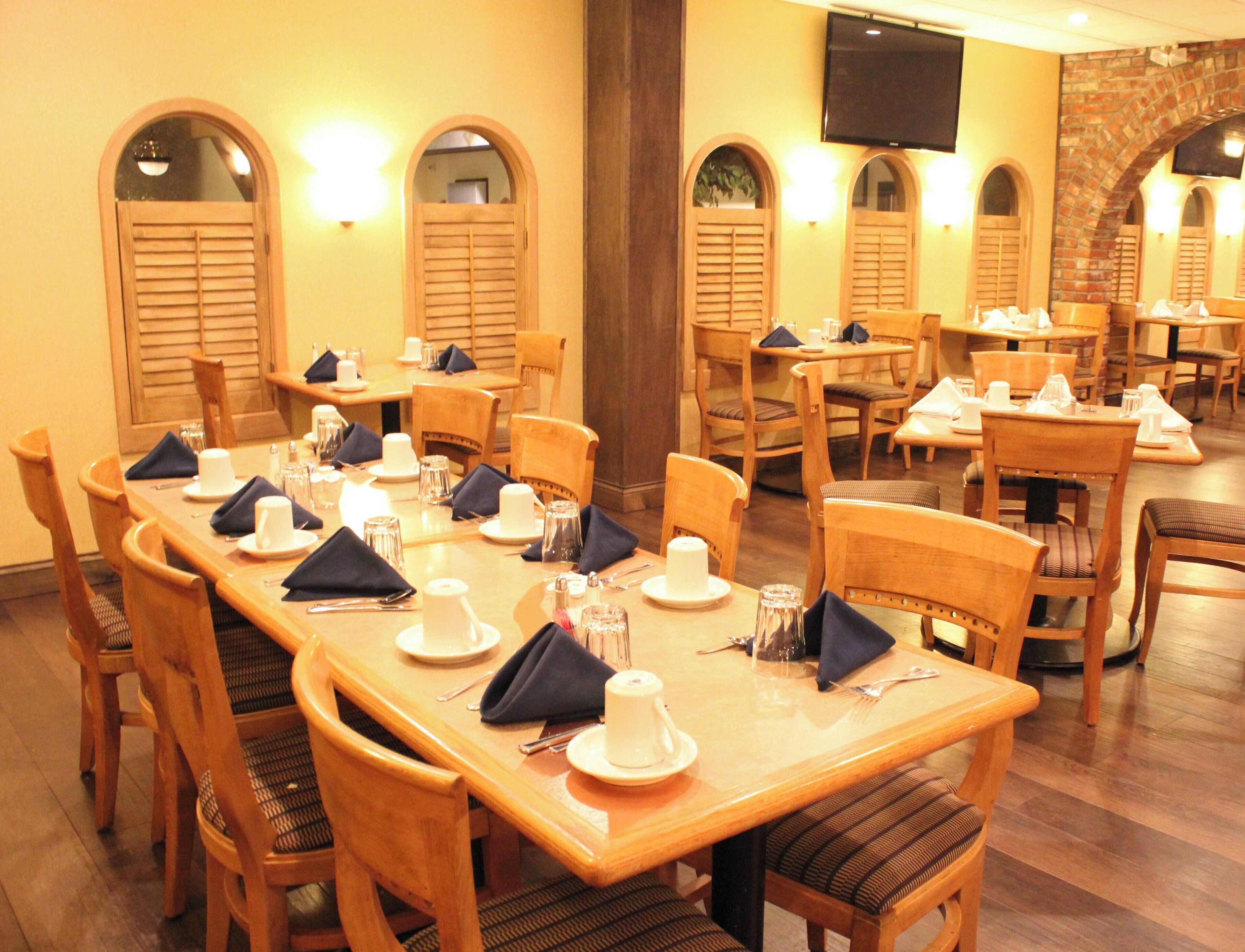 Un restaurant avec plusieurs tables dressées pour le service, des chaises en bois et un téléviseur fixé au mur.
