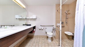 A modern bathroom with a white sink, mirror, and toilet. There are shelves with toiletries and a shower with a handheld showerhead. - Holiday Inn Great Falls- Convention Center by IHG (Great Falls)
