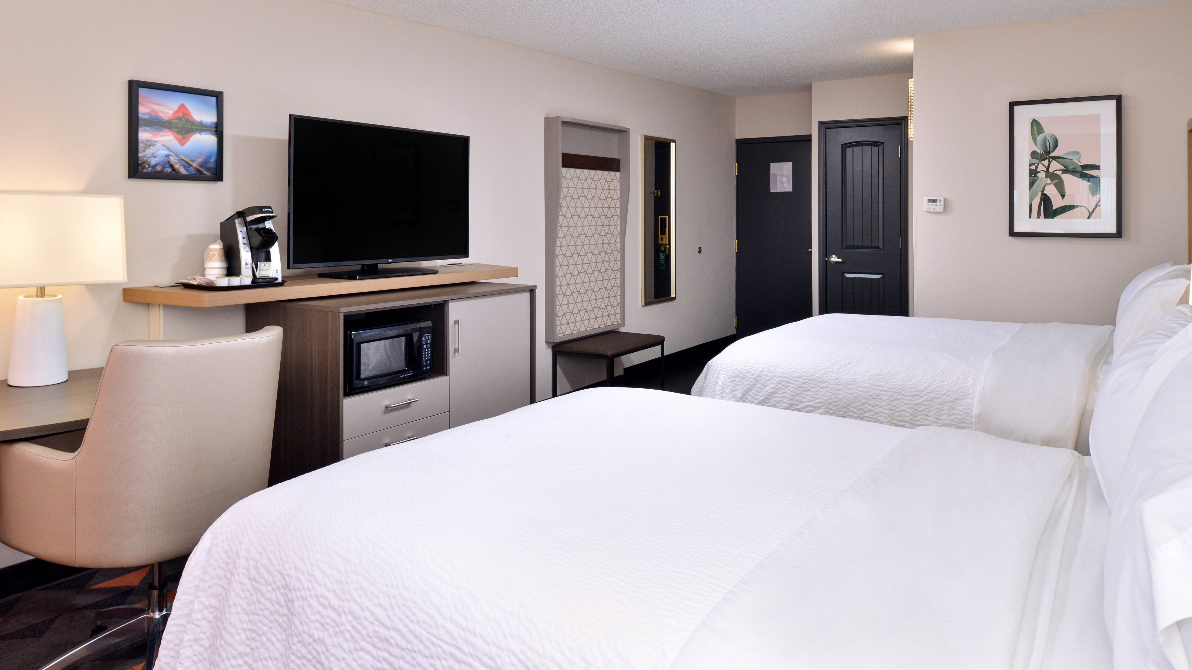 A hotel room with two beds, a desk with a flat-screen TV, a microwave, a chair, and a door.