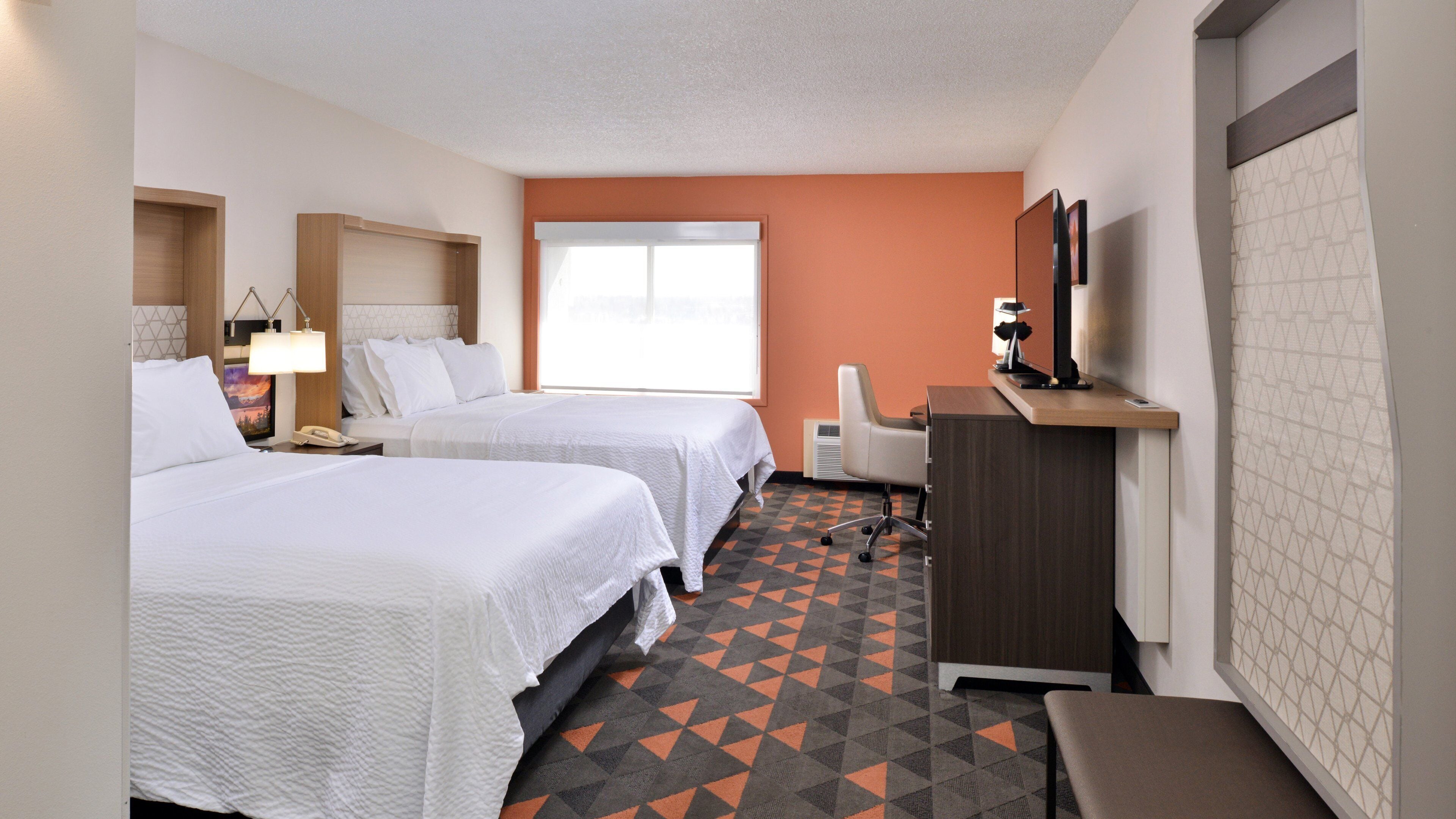 A hotel room with two beds, a desk, a chair, a TV, and a window.