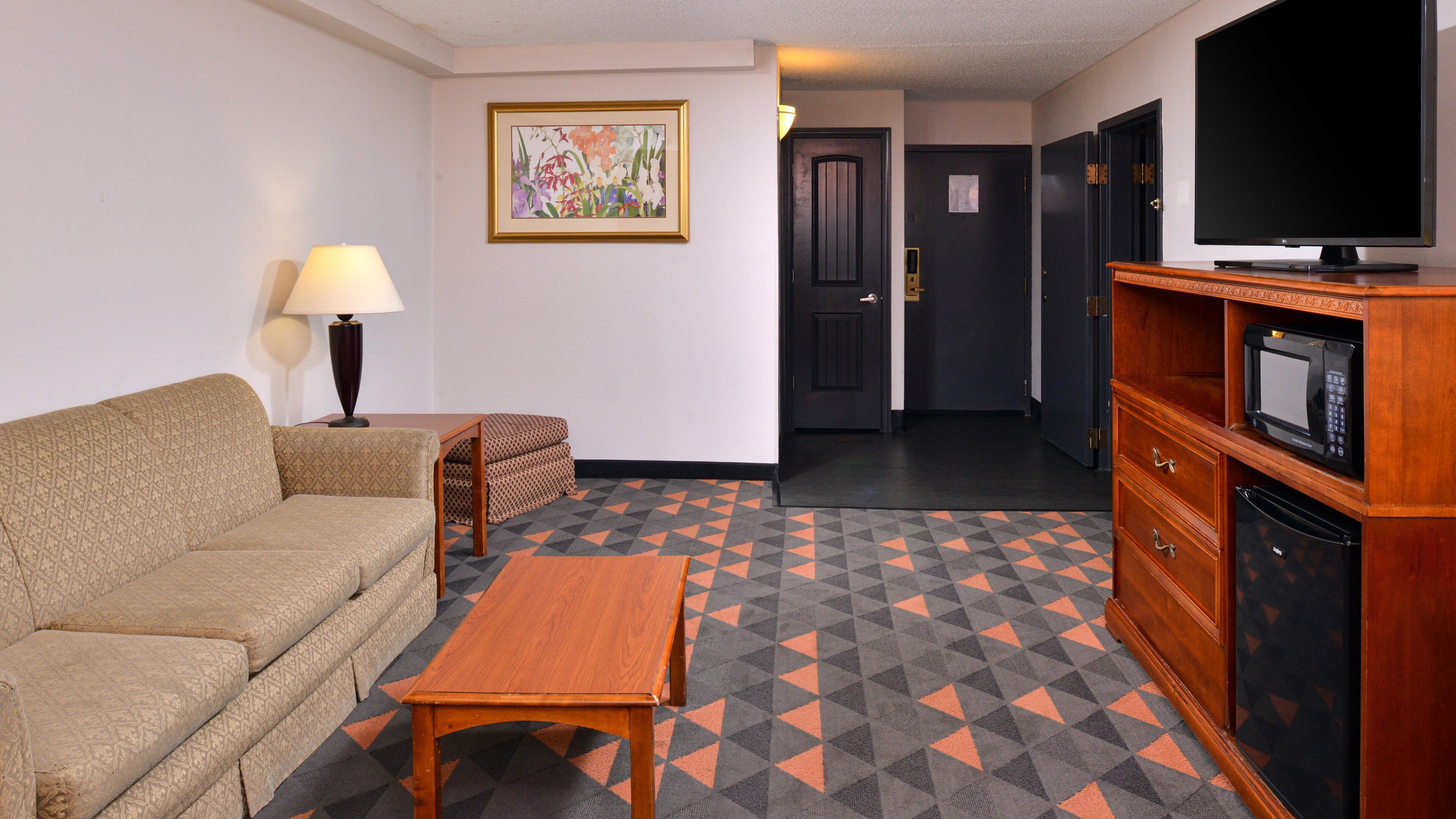 A hotel room with a sofa, a small table, a lamp, a framed picture on the wall, a television, and a microwave on a wooden cabinet.