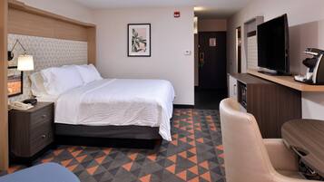 A hotel room with a bed, bedside table, lamp, TV, and a chair.